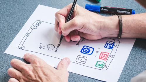 A person draws a mobile phone interface on a piece of paper. 